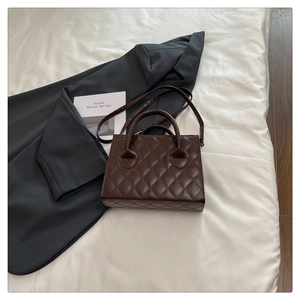 Detail of dark brown quilted leather handbag featuring round dual handles and a slim strap