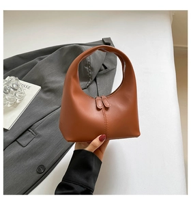 Detail of warm brown half-moon handbag with dual zippers and unique arc handle design