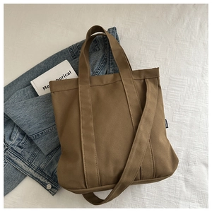 Vue détaillée du sac cabas en toile marron avec étiquette mode sur un fond en tissu blanc