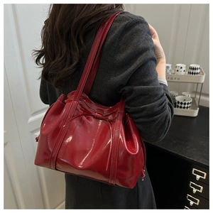 Red patent leather underarm bag with bow detail shown on a model in a modern interior