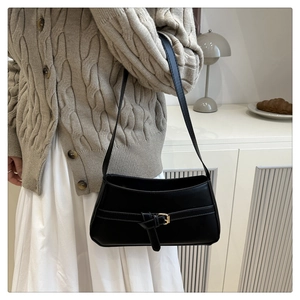 Detail of minimalist black faux leather shoulder bag with decorative buckle on a model