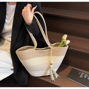 Detail of woven straw tote bag featuring a tricolor gradient pattern and tassel charm