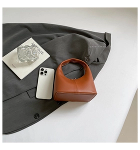 Top view of a mini orange semi-circular PU leather handbag on a gray suit fabric background
