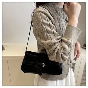 Detail of a minimalist black leather underarm bag with decorative buckle on a model