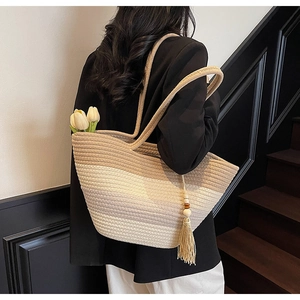 Detail shot of oversized striped woven straw tote bag featuring decorative fringe tassel charm