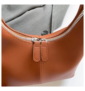 Detail of premium brown leather handbag featuring dual silver zippers and precise stitching