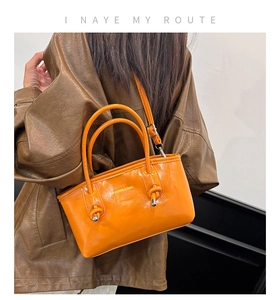 Detail of bright orange bucket bag with knotted handles and metallic decor details