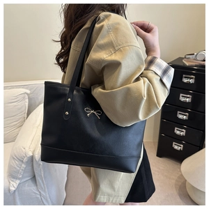 Detail of black leather tote bag with gold bow clasp and metal studs on a female model