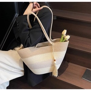 Detail of woven straw tote bag featuring tassel accents and a gradient beige texture