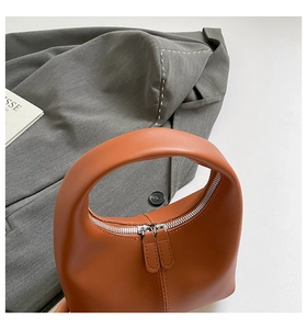 Detail of a brown crescent handbag with matte leather texture and smooth metal zippers