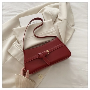 Detail of dark red matte leather baguette bag with golden buckle on a beige blazer