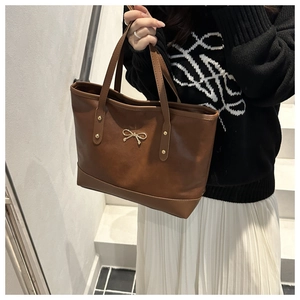 Brown leather tote bag featuring a gold metal bow detail and elegant rivet handles