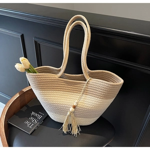 Detail of gradient straw tote bag featuring woven texture and decorative tassel with wooden beads