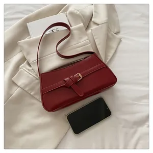 Detail of burgundy leather shoulder bag with buckle strap on a beige blazer