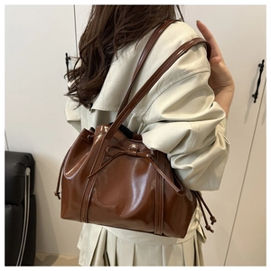 Close-up of brown glossy PU leather tote bag with a bow detail and drawstring side