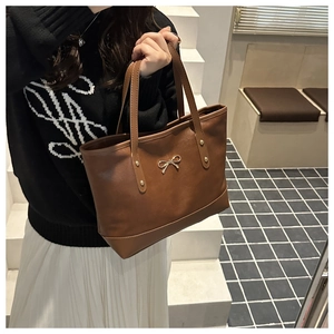 Detail of a brown tote bag featuring a golden bow metal buckle and sturdy gold rivets