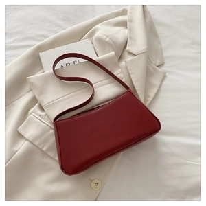 Deep red faux leather shoulder bag on white blazer with arts book background