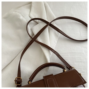 Close-up of brown leather handbag with gold metal buckles and adjustable strap