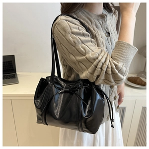 Detail of a black patent leather shoulder bag with bow knot and side drawstring pleats