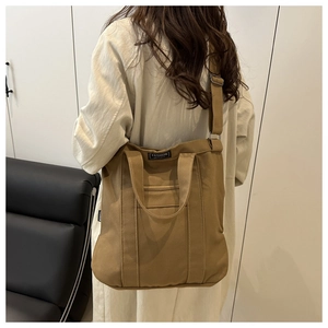 Rear view of a model styling a large brown canvas tote bag with adjustable shoulder straps