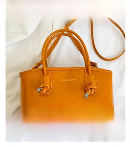 Detail of orange high-gloss handbag with fashion logo and unique knotted handle design