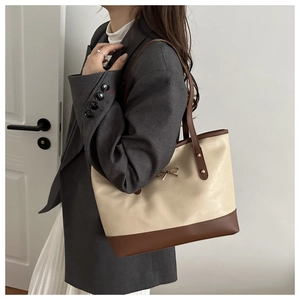 Detail of a large beige tote bag with brown straps and a golden metal bow decoration