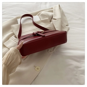 Close-up of a burgundy matte leather underarm bag with buckle on a beige blazer