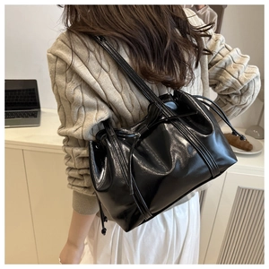 Detail of black glossy patent leather shoulder bag with decorative drawstring and bow