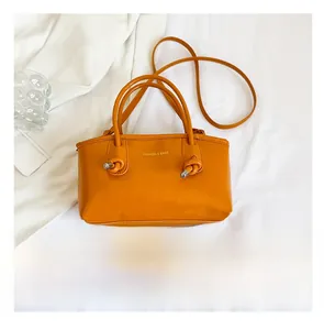 Detail of orange square handbag with double handles and fashion logo in a bright setting