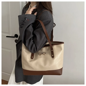 Detail of a large two-tone tote bag with gold bow buckle and brown leather accents