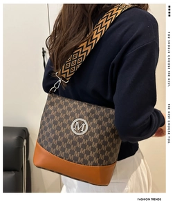Detail view of stylish monogram crossbody bag with wide strap and silver M logo
