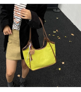 Detail of yellow-green suede tote bag with brown leather trim and bear charm accessory
