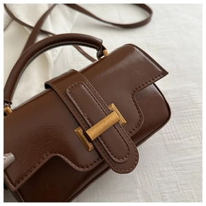 Detail view of deep brown vintage handbag with gold clasp on textured white fabric