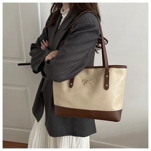 Detail of two-tone tote bag with white PU leather and gold bow metallic hardware accessory