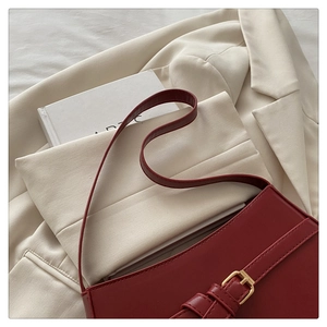 Detail of burgundy leather underarm bag featuring a gold buckle and slim strap