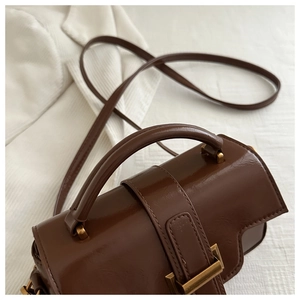 Detail of glossy brown leather crossbody bag with vintage gold metal buckle closure