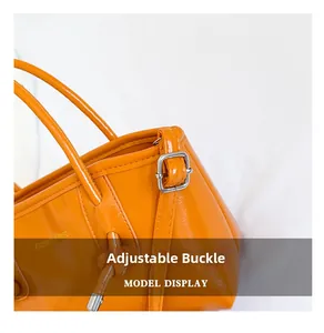 Detail view of the adjustable silver buckle and orange faux leather strap on bucket bag