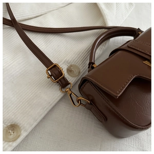 Close-up of vintage brown leather bag featuring bronze metal buckle and adjustable strap