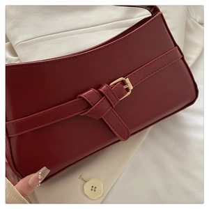 Close-up of deep red faux leather underarm bag with gold pin buckle detail