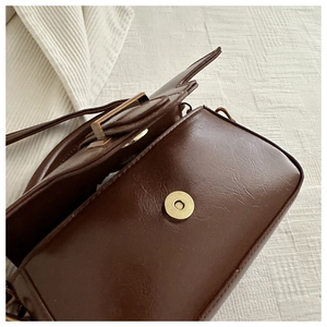 Close-up of dark brown glossy wax leather bag with golden magnetic snap closure