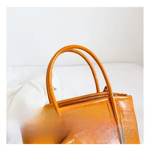 Detail of bright orange glossy tote bag showing durable handles and smooth leather texture