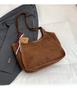 Close-up of brown suede bucket bag with leather handles, plush bear and ribbon detail