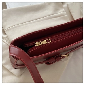 Detail of burgundy shoulder bag with matte gold zipper and knotted strap design