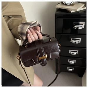 Close-up of a dark brown glossy crossbody bag with vintage gold buckle and plaid lining