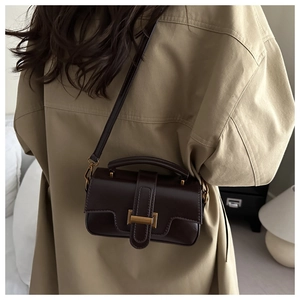 Detail of dark brown leather crossbody bag with vintage gold buckle on trench coat