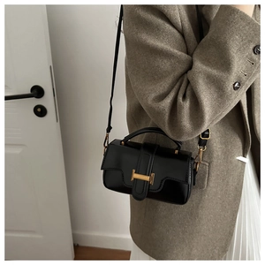 Close-up of black matte leather crossbody bag with gold buckle on wool coat outfit