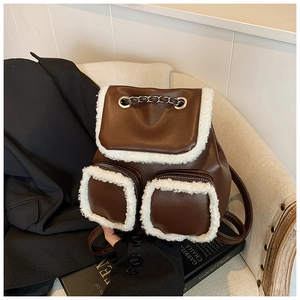 Detail of dark brown backpack with white faux fur trim and silver chain on sofa