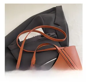 Detail of caramel leather shoulder strap with gold buckle and black stitching on a bucket bag