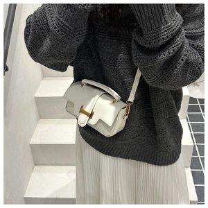 Détail d'un sac blanc en cuir avec boucle H dorée et design élégant à rabat ondulé