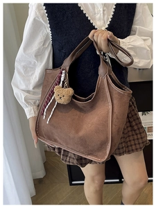 Close-up of deep brown suede bucket bag with leather handle and plush bear charm